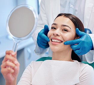 Smiling patient holding a mirror while dentist checks teeth at a dental clinic.