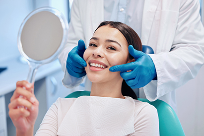 Smiling patient holding a mirror while dentist checks teeth at a dental clinic