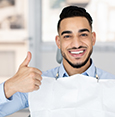 Happy dental patient smiling and showing thumbs up after successful treatment at the clinic